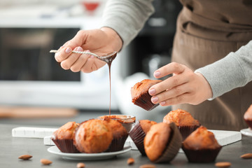 Woman pouring chocolate sauce on tasty cupcake, closeup