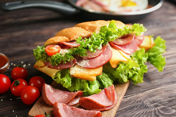 Wooden board with tasty croissant sandwich on table