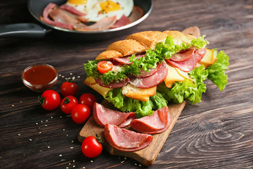 Wooden board with tasty croissant sandwich on table