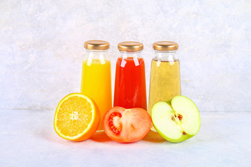 Bottles with fresh orange, apple, tomato juice on a gray concrete table.