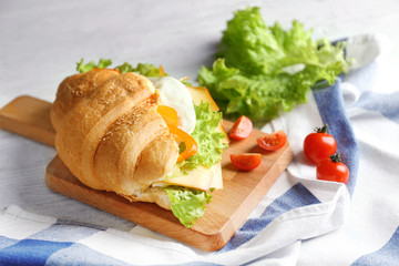 Wooden board with tasty croissant sandwich on table
