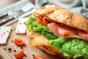 Tasty croissant sandwich on wooden board, closeup