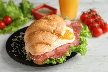 Plate with tasty croissant sandwich and glass of juice on table