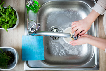 Young woman hands cleaning some dirty dishes by sponge and detergent