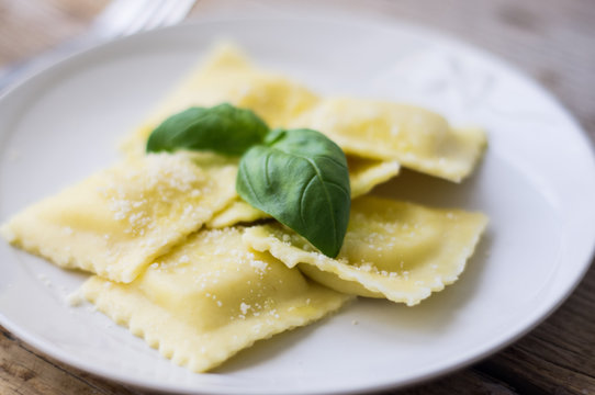 Plate of ravioli with ricotta cheese, basil and grated parmesan cheese on top on wooden table
