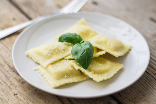 Plate of ravioli with ricotta cheese, basil and grated parmesan cheese on top on wooden table