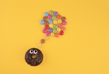 Colorful glazed donuts with funny eyes on yellow background.