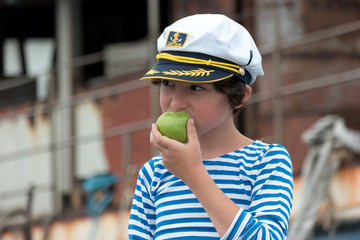 Portrait of a boy in a vest (Telnyashka) and captain's cap. In his hand a green apple.