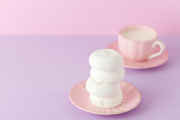 Violet pastel horizontal banner with - white zephyr sweets on pinkplate and cup of coffee with milk.