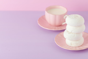 Pastel violet and pink horizontal banner with copy space - white zephyr on plate and cup of coffee with milk.