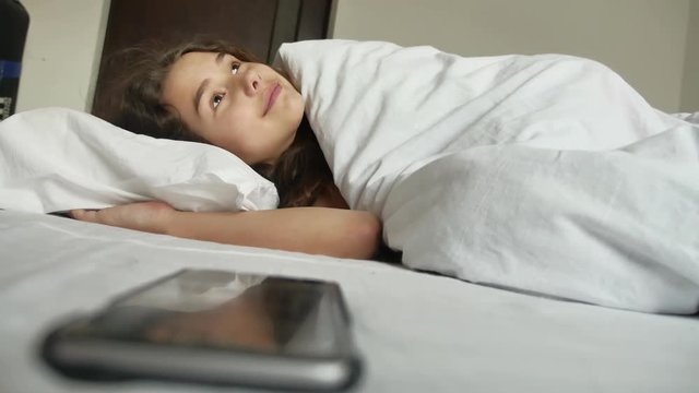 little girl indoors is sleeping in bed. little girl wakes up and looks at the smartphone alarm clock lifestyle