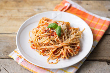 Homemade Italian pasta spaghetti with tomato sauce, fresh herbs and grated parmesan cheese on wooden rustic table