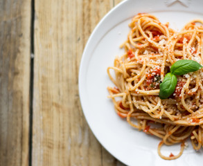 Homemade Italian pasta spaghetti with tomato sauce, fresh herbs and grated parmesan cheese on wooden rustic table