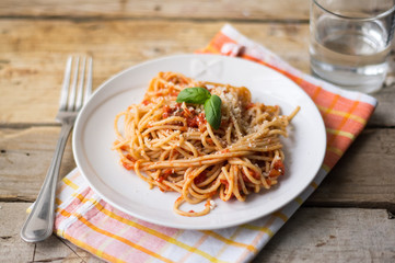 Homemade Italian pasta spaghetti with tomato sauce, fresh herbs and grated parmesan cheese on wooden rustic table