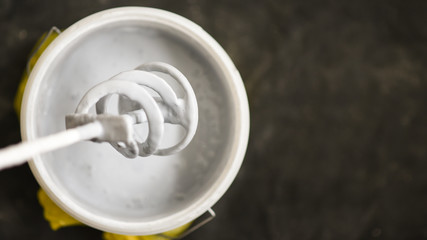 Paddle mixer over the bucket with white paint for wall, DIY tools and accessory, workflow close up,...