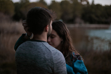 A cute spanish couple having a nice afternoon hugging and kissing each other in a park in front of a lake in Seville, Spain.