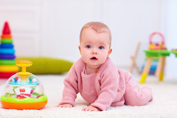 cute little baby girl crawling on the carpet among the development toys