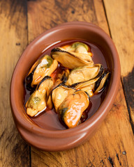 clay bowl with mussels in sauce, on dark wooden board