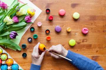 Woman paints easter eggs, wood easter background, top view