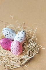 View of a straw nest with colorful pink and white freckled Easter eggs on cardboard background, Happy Easter background