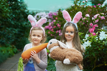 Children play with toy rabbit. Laughing child at Easter egg hunt with pet bunny. Little toddler girl playing with animal in the garden.