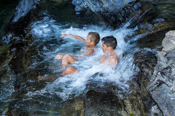 two boys are bathing in a mountain small waterfall