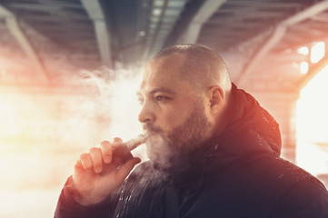 Vape man. Young guy vaping electronic cigarette or vape pen at urban background, modern lifestyle...