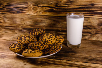 Plate with chocolate chip cookies and a glass of milk on a wooden table