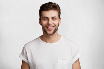 Horizontal shot of handsome young guy with blue eyes and bristle, has positive expression, being praised by someone, dressed casually, isolated over white studio background. Emotions concept
