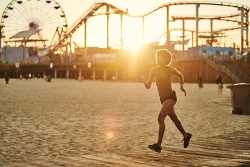 athletic african american woman jogging on boardwalk at sunset - obrazy, fototapety, plakaty