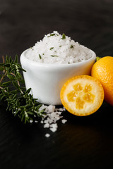 Coarse sea salt flakes, so called Fleur de Sel, infused with thmye leaves and kumquat orange juice in small white bowl for seasoning in the kitchen on dark slate background