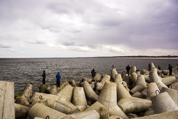 Fototapeta na wymiar Many fishermen catch fish at the sea standing on big boulders.