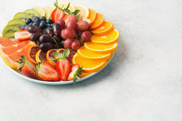 Variety of fruits and berries in rainbow colours platter close up, strawberries, grapes, blueberries, kiwis, grapefruit, grapefruit on off white table, copy space for text, selective focus