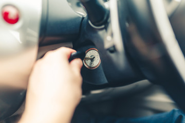 Hand s man plug in a key starting the engine of a car. The hand inserts the key into the ignition and starts the car. Hand put the car key to the keyhole starting the car. Stylish Toned photo