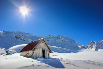Winter landscape with wooden toolshed and Fagaras Mountains covered in thick layer of snow at Balea lake, Sibiu county, Romania