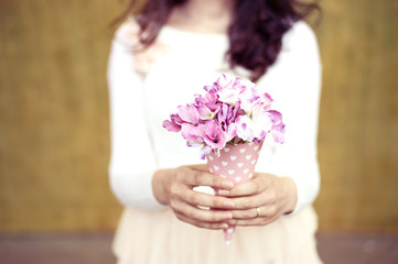 Close up to woman's hands holding a pink paper cone with hydrangea flowers