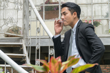 Handsome young man wear suit and white shirt smoking cigarette on the stairs. He standing outside...