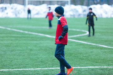  boy in red uniform -football player plays soccer on the green field in the winter
