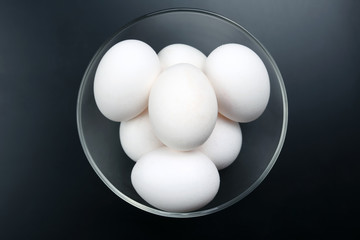 white chicken eggs lying on the plate on a dark background.