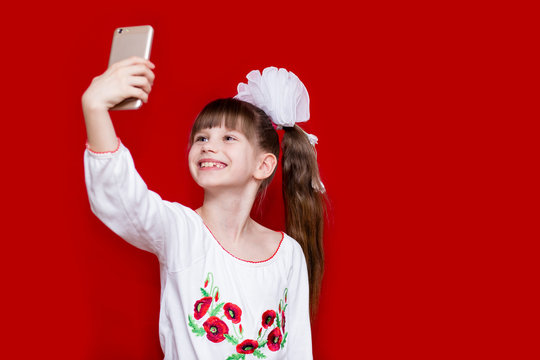 A cute little girl in white bows hold telephone and take picture on red background. Communication concept
