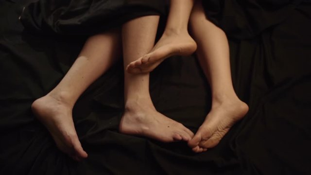 Portrait cropped legs of man and woman lying in bed together at night, hugging and expressing loving feelings slow motion