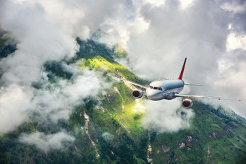 Aerial view of aircraft. Airplane is flying in clouds over mountains with forest at sunset....