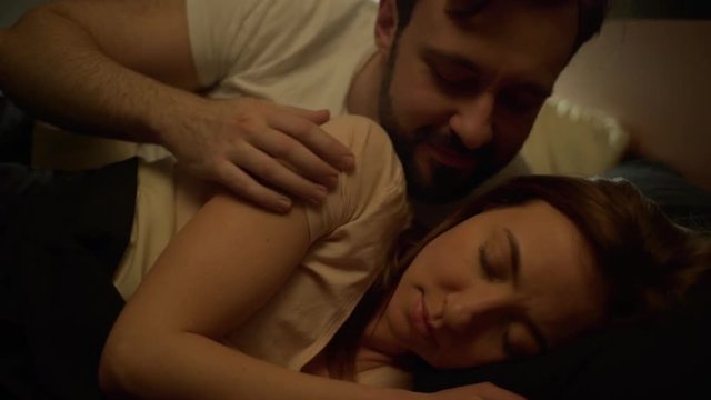 Portrait of married couple wife and husband having european appearance resting in bed together at night, man hugging his beloved woman when sleeping slow motion
