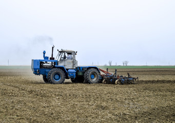 Obraz premium Lush and loosen the soil on the field before sowing. The tractor plows a field with a plow