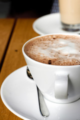 Close up of large cup of hot chocolate with frothy milk or cappucino and glass of milky coffe, cafe auf lait or latte in background