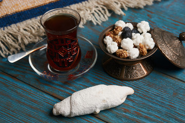 Biscuits with walnuts and powdered sugar, oriental sweets mutaki on rustic wooden table with traditional turkish tea and sweet snack in silver bowl, top view