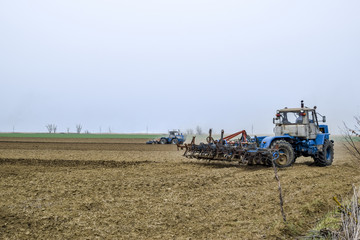 Fototapeta premium Lush and loosen the soil on the field before sowing. The tractor plows a field with a plow