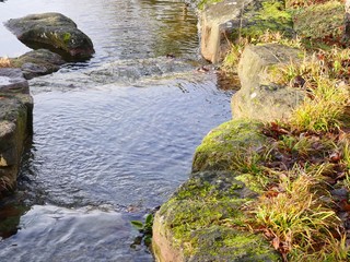 Small creek flows through a rocky environment, The stones are partly overgrown with moss and grass