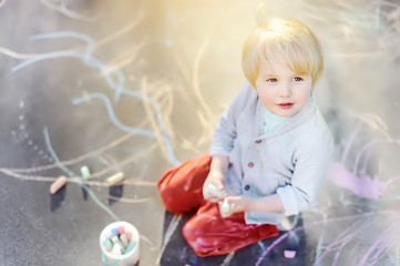 Naklejka premium Happy little kid boy drawing with colored chalk on asphalt.