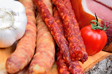 Sausages with prosciutto crudo and garlic and cherry tomatoes on a wood cutting board